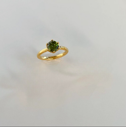 Gold ring with a green gemstone on a light grey background