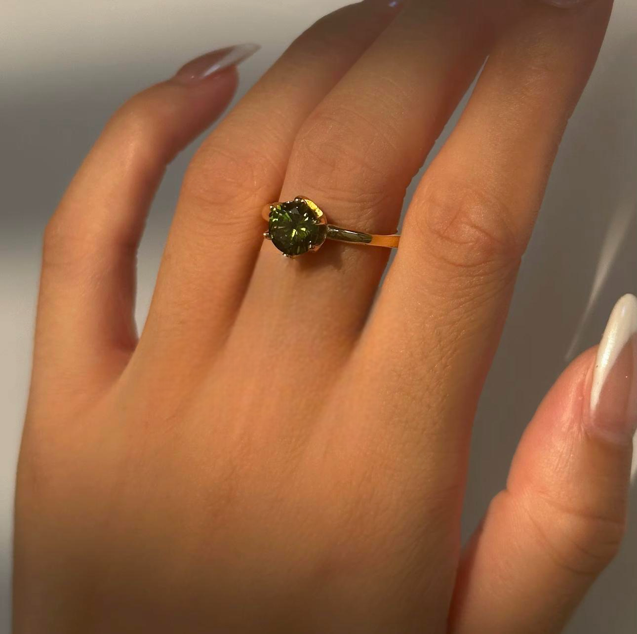 Close-up of a hand wearing a ring with a green gemstone on a neutral background