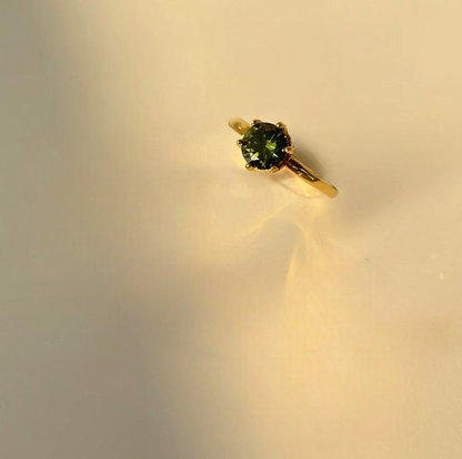 Gold ring with a green gemstone on a beige background