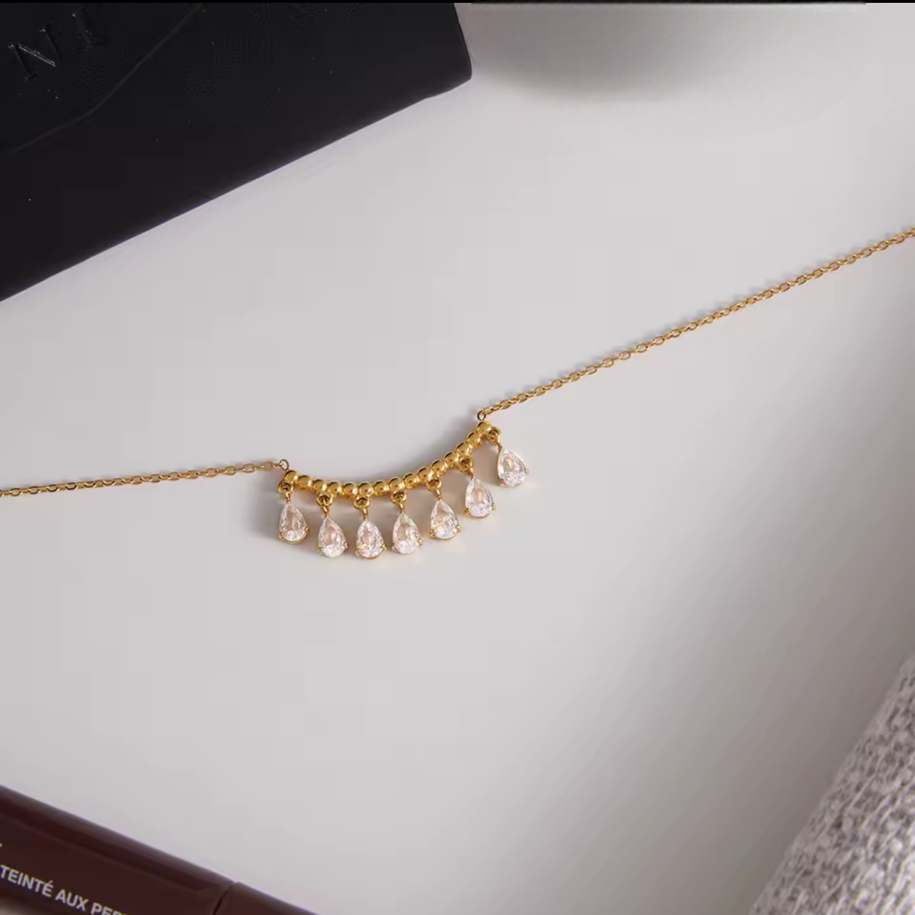 gold necklace featuring a row of pear shaped gemstones pictured on a neutral background