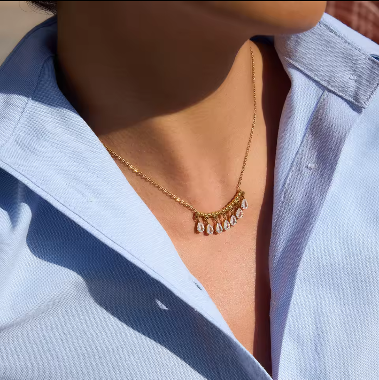 gold necklace featuring a row of pear shaped gemstones pictured being worn around the neck