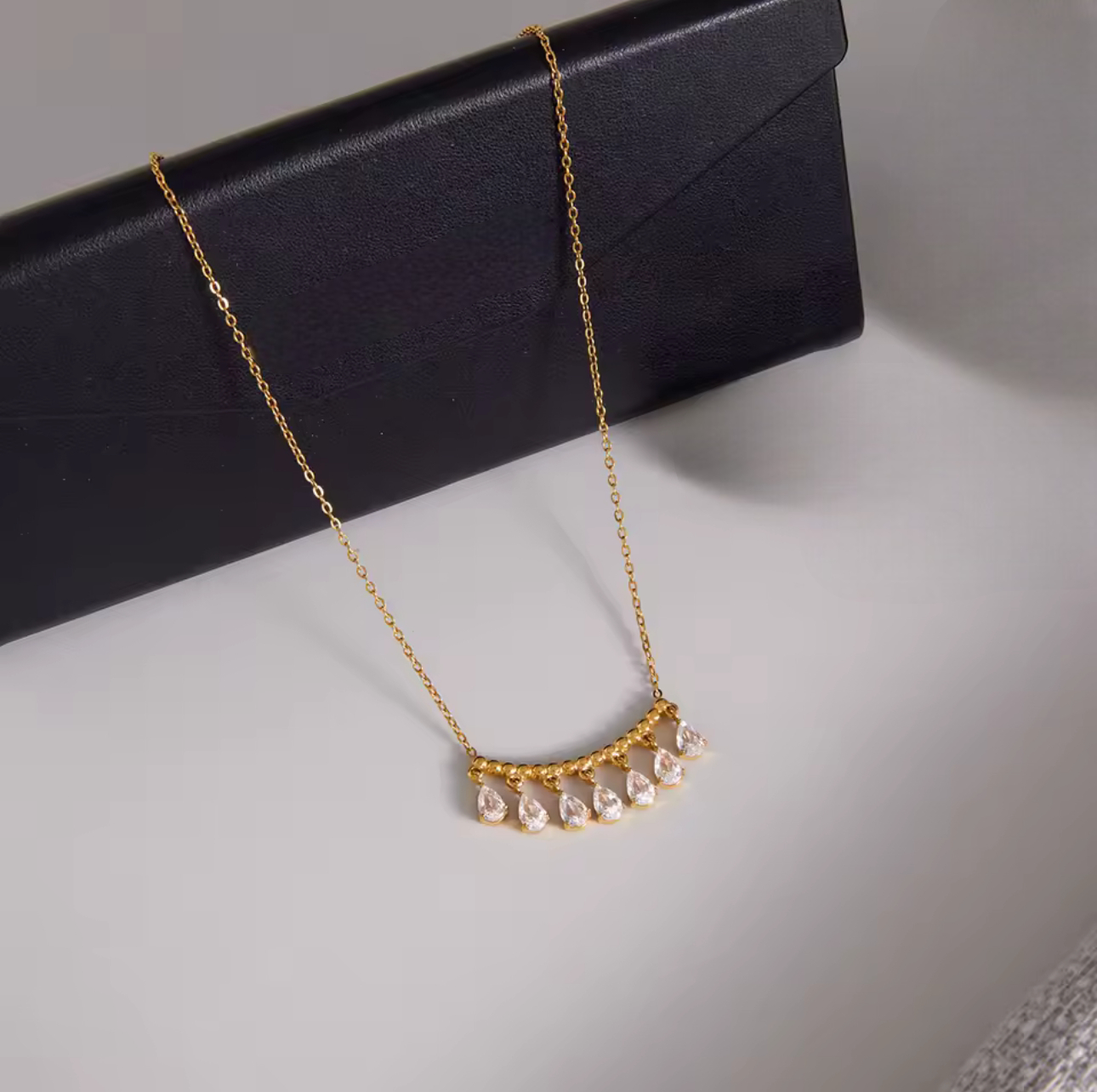 gold necklace featuring a row of pear shaped gemstones pictured on a neutral background