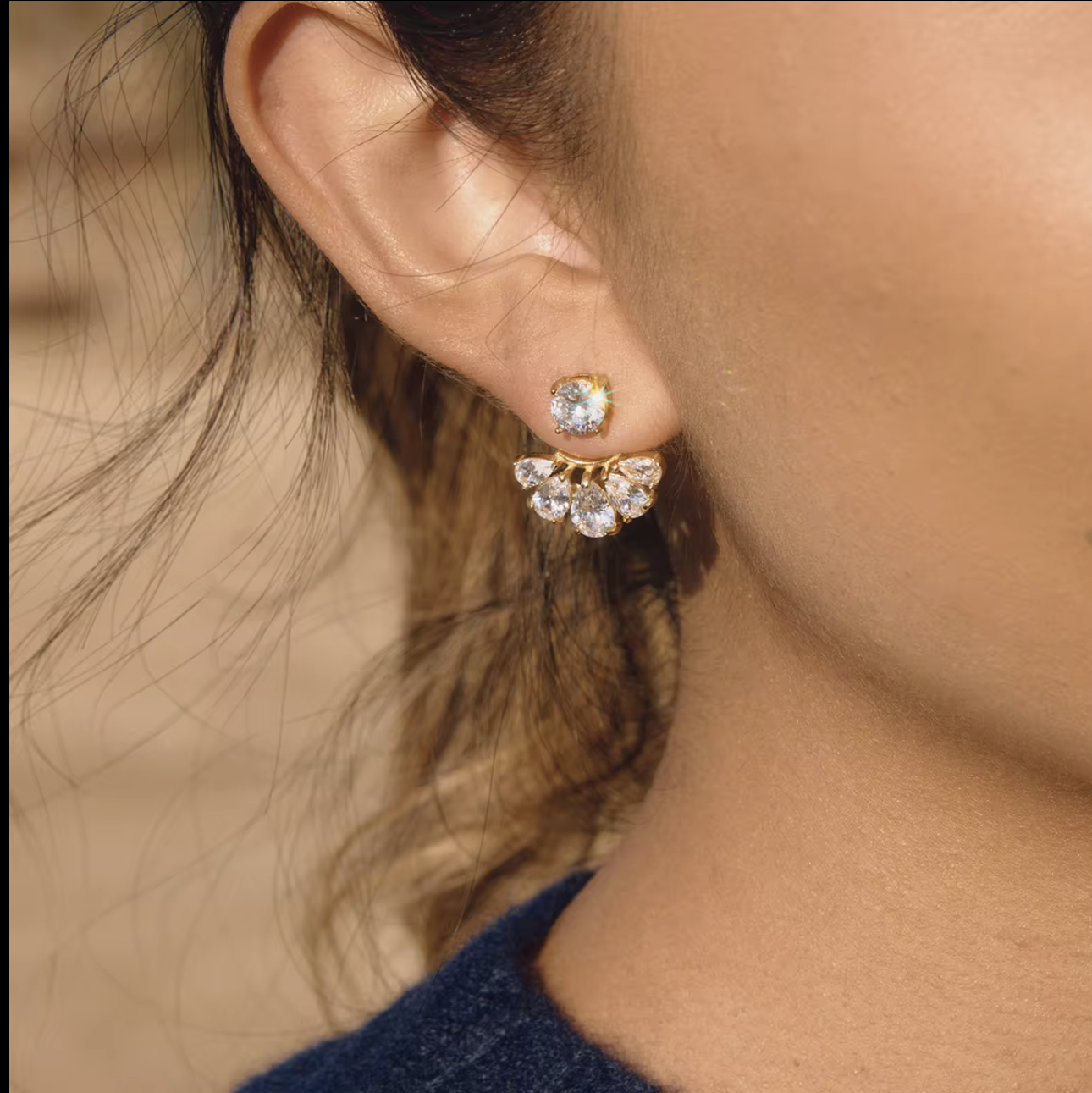 gold earrings with clear pear shaped gemstones pictured being worn in the ear