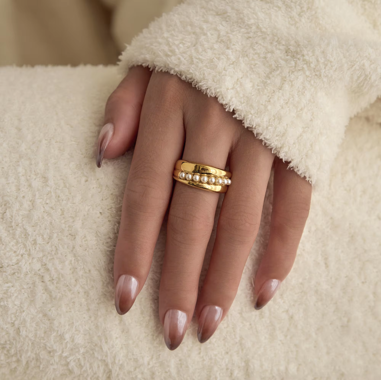 Hand wearing a gold ring on a beige background