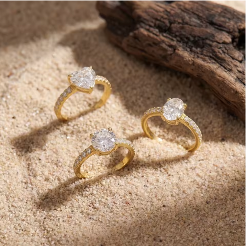 Gold rings with heart-shaped and round gemstones on a sandy surface