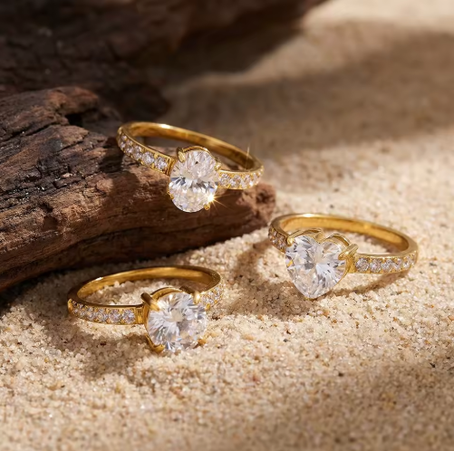 Three gold rings with diamond stones on a sandy surface