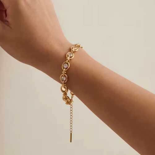 Gold bracelet with small diamonds on a wrist against a beige background