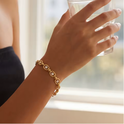 Hand wearing a gold bracelet holding a glass, with a blurred background