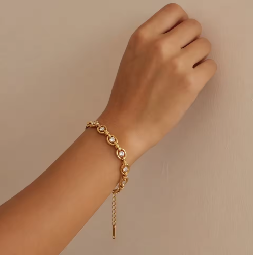 Gold bracelet with clear gemstones on a wrist against a beige background