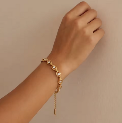 Gold bracelet with clear gemstones on a wrist against a beige background