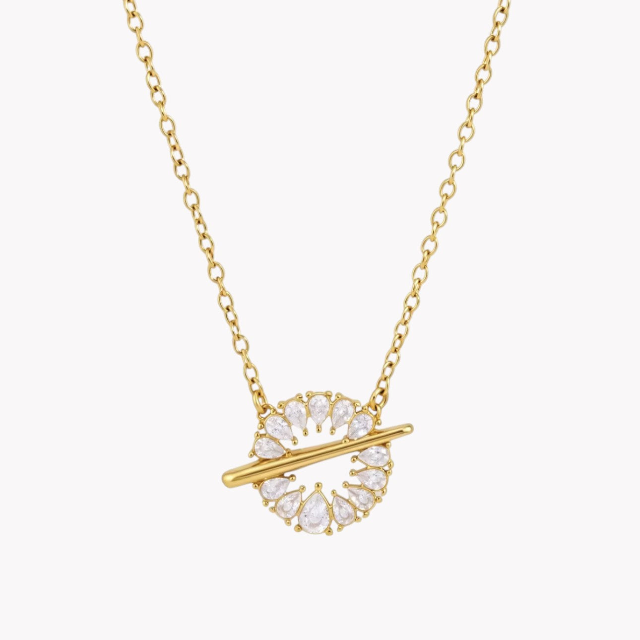 A gold chain necklace with a circular pendant featuring clear teardrop-shaped crystals and a horizontal gold bar, shown on a light gray background.