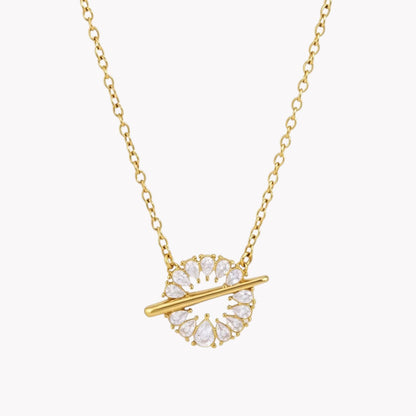 A gold chain necklace with a circular pendant featuring clear teardrop-shaped crystals and a horizontal gold bar, shown on a light gray background.