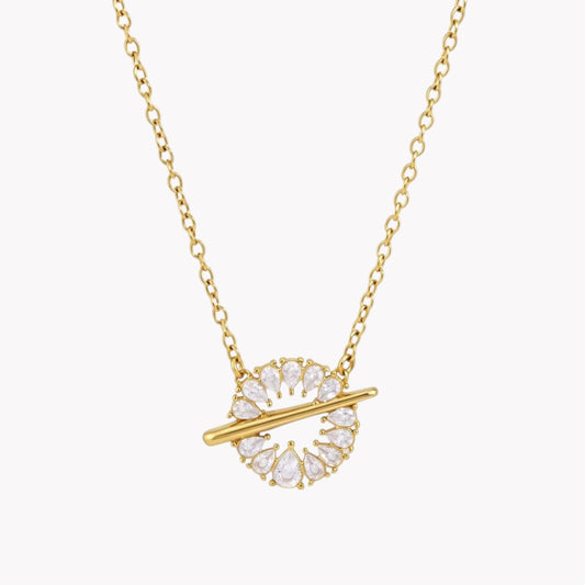 A gold chain necklace with a circular pendant featuring clear teardrop-shaped crystals and a horizontal gold bar, shown on a light gray background.