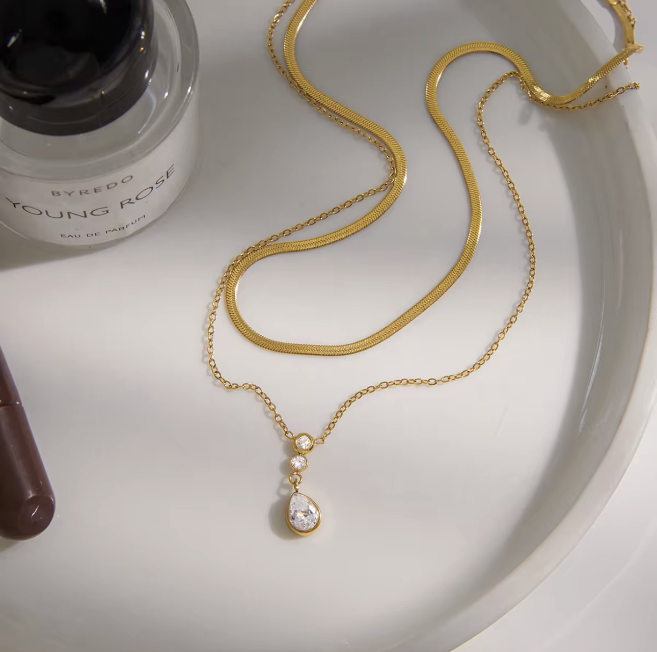 Double layer necklace featuring a top layer snake chain with bottom longer layer with pear shaped gemstone pendant pictured on a light background