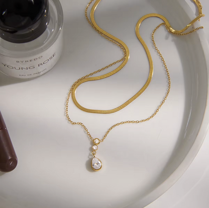 Double layer necklace featuring a top layer snake chain with bottom longer layer with pear shaped gemstone pendant pictured on a light background