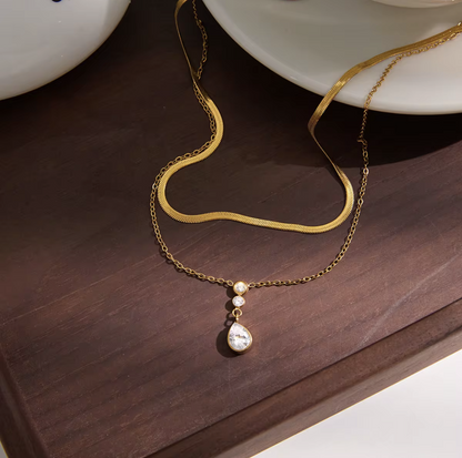 Double layer necklace featuring a top layer snake chain with bottom longer layer with pear shaped gemstone pendant pictured on a dark wooden background