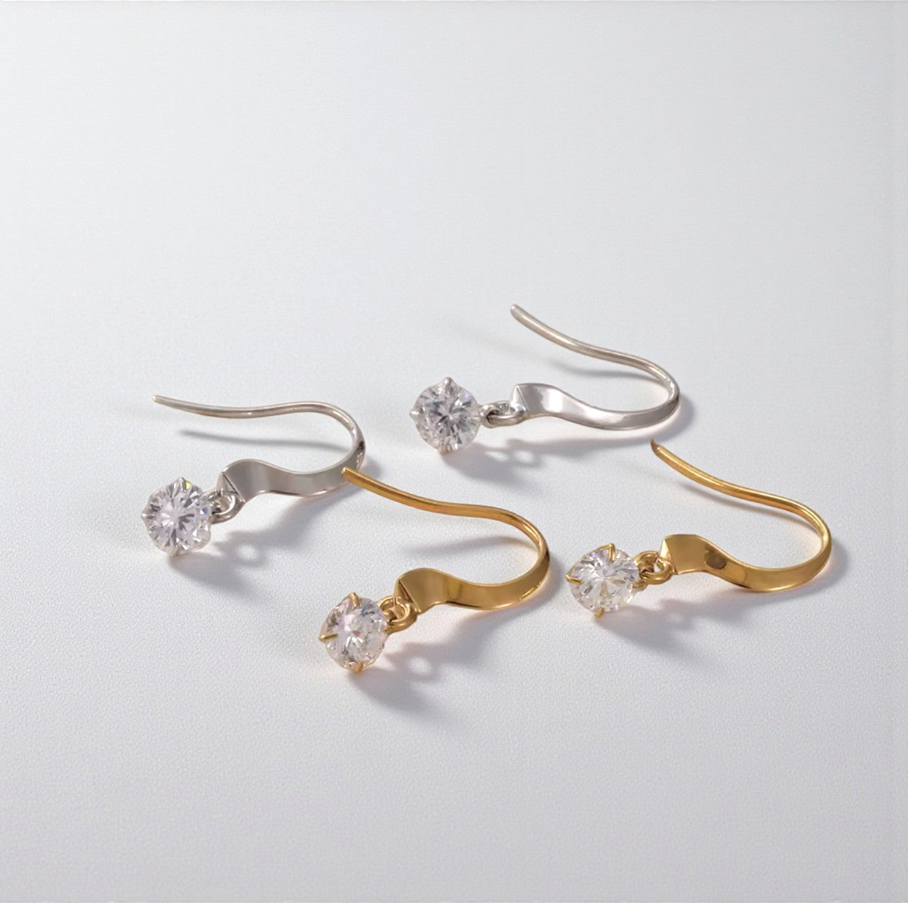 Pair of gold and silver earrings with clear gemstones on a light gray background