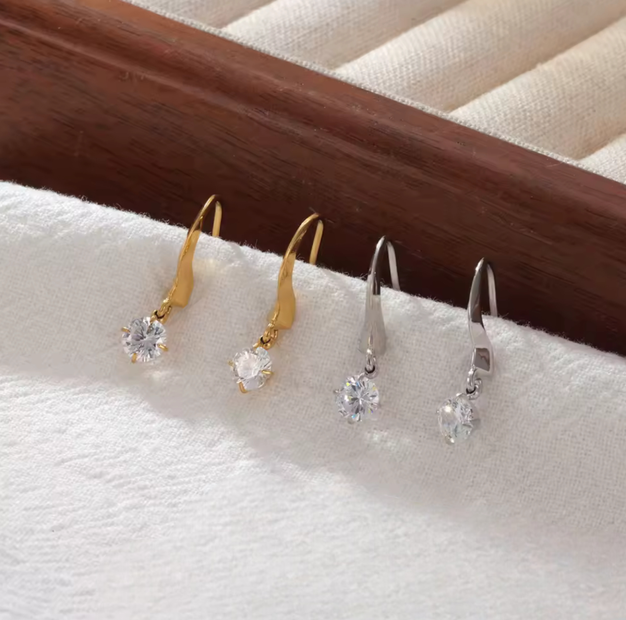 Four pairs of earrings in gold and silver on a white surface with a wooden background