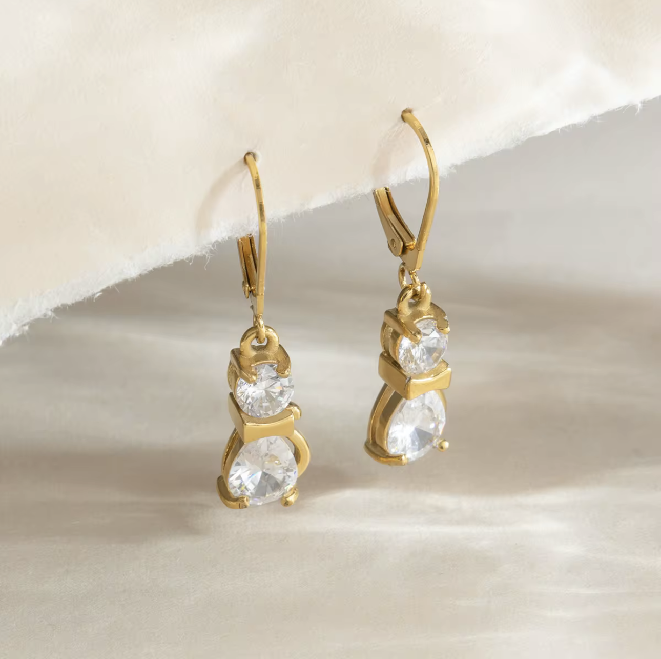 Gold earrings with clear gemstones on a beige background