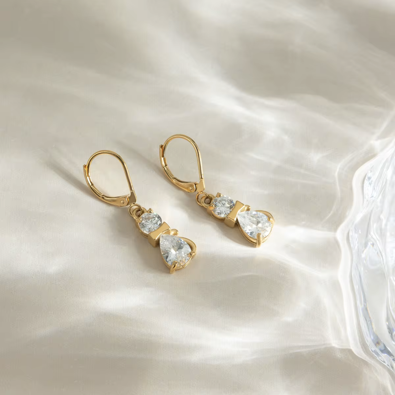 Gold earrings with clear gemstones on a soft white fabric background