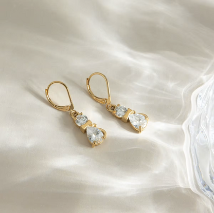 Gold earrings with clear gemstones on a soft white fabric background