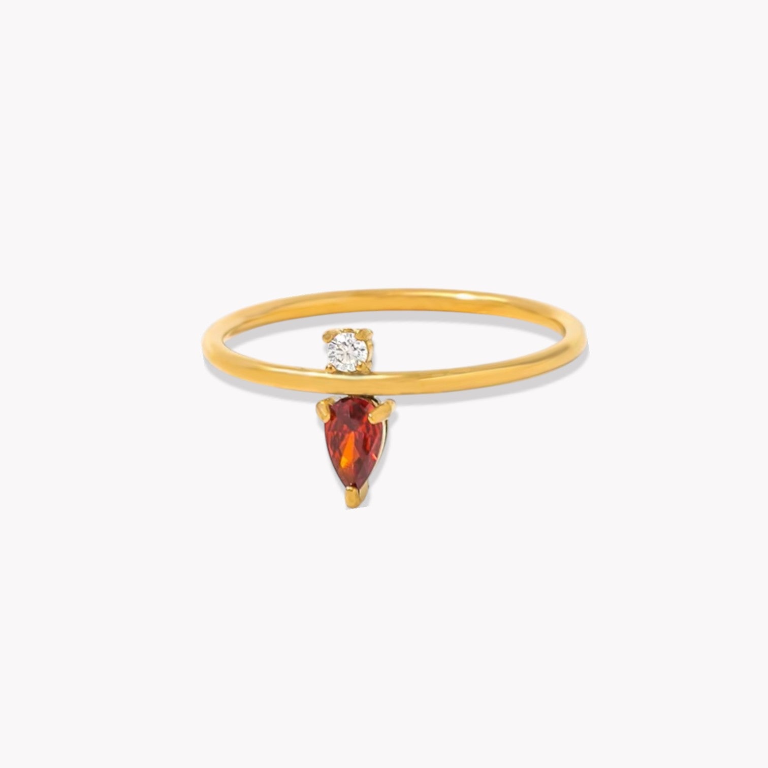 Gold ring with a red pear shaped gemstone and a clear round gemstone on a white background