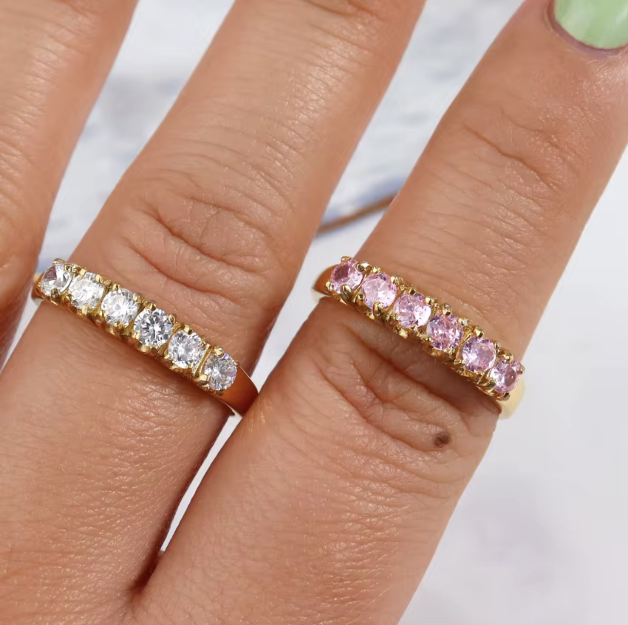 Two gold rings with gemstones on fingers against a white background