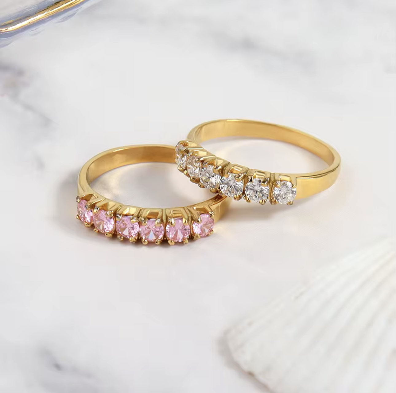 Two gold rings with gemstones on a marble surface