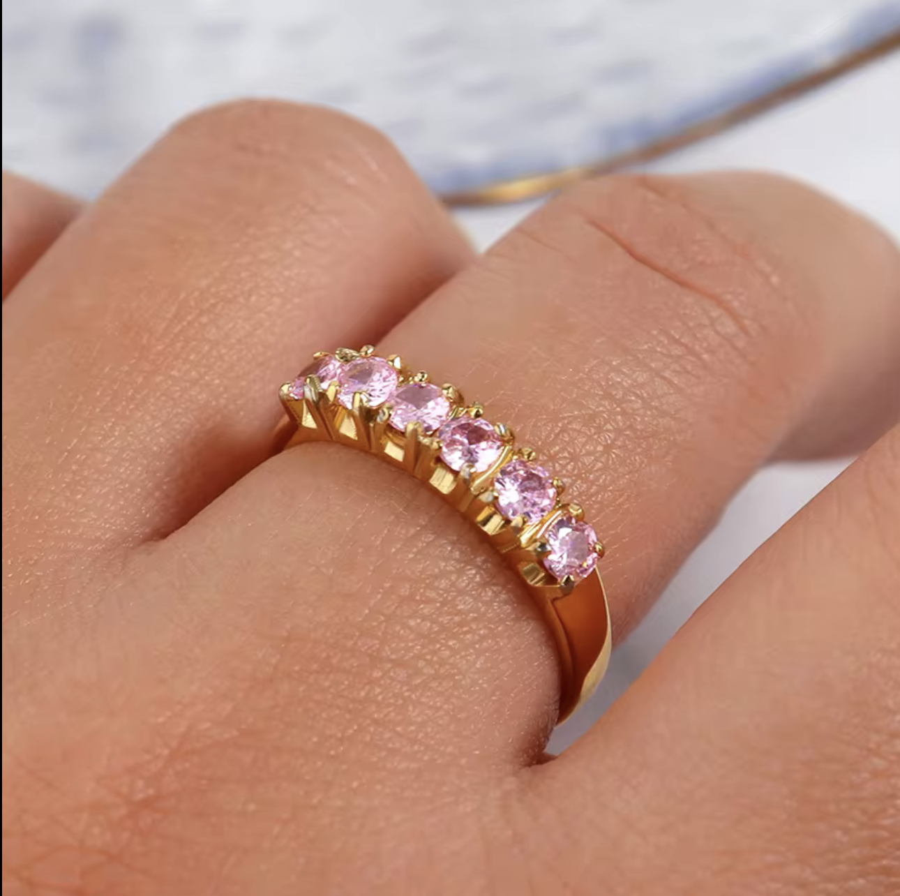 Gold ring with pink gemstones on a finger against a neutral background