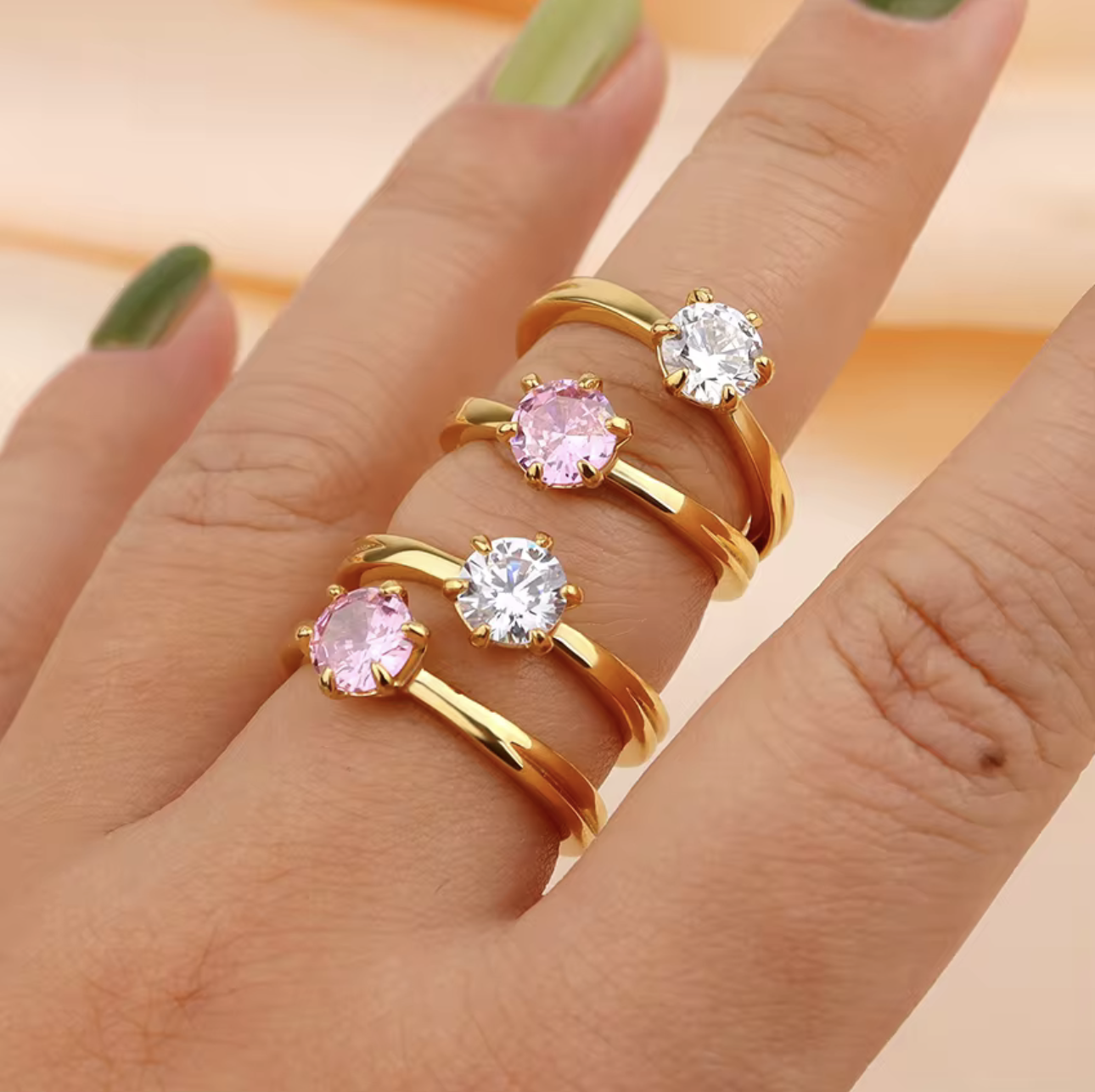 Gold rings with pink and clear gemstones on a hand against a peach background