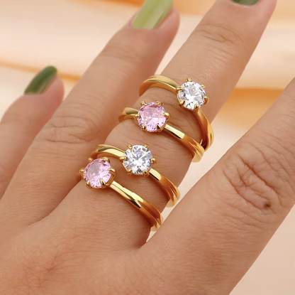Gold rings with pink and clear gemstones on a hand against a peach background