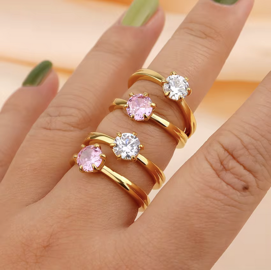 Gold rings with pink and clear gemstones on a hand against a peach background