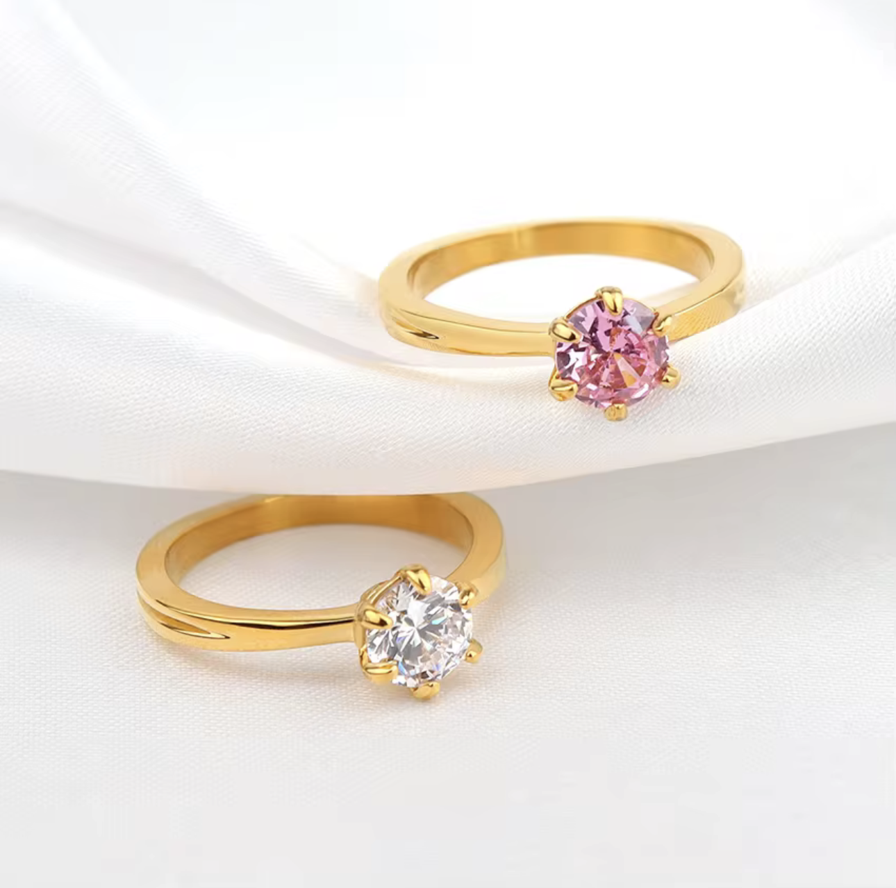 Two gold rings with pink and clear gemstones on a white background