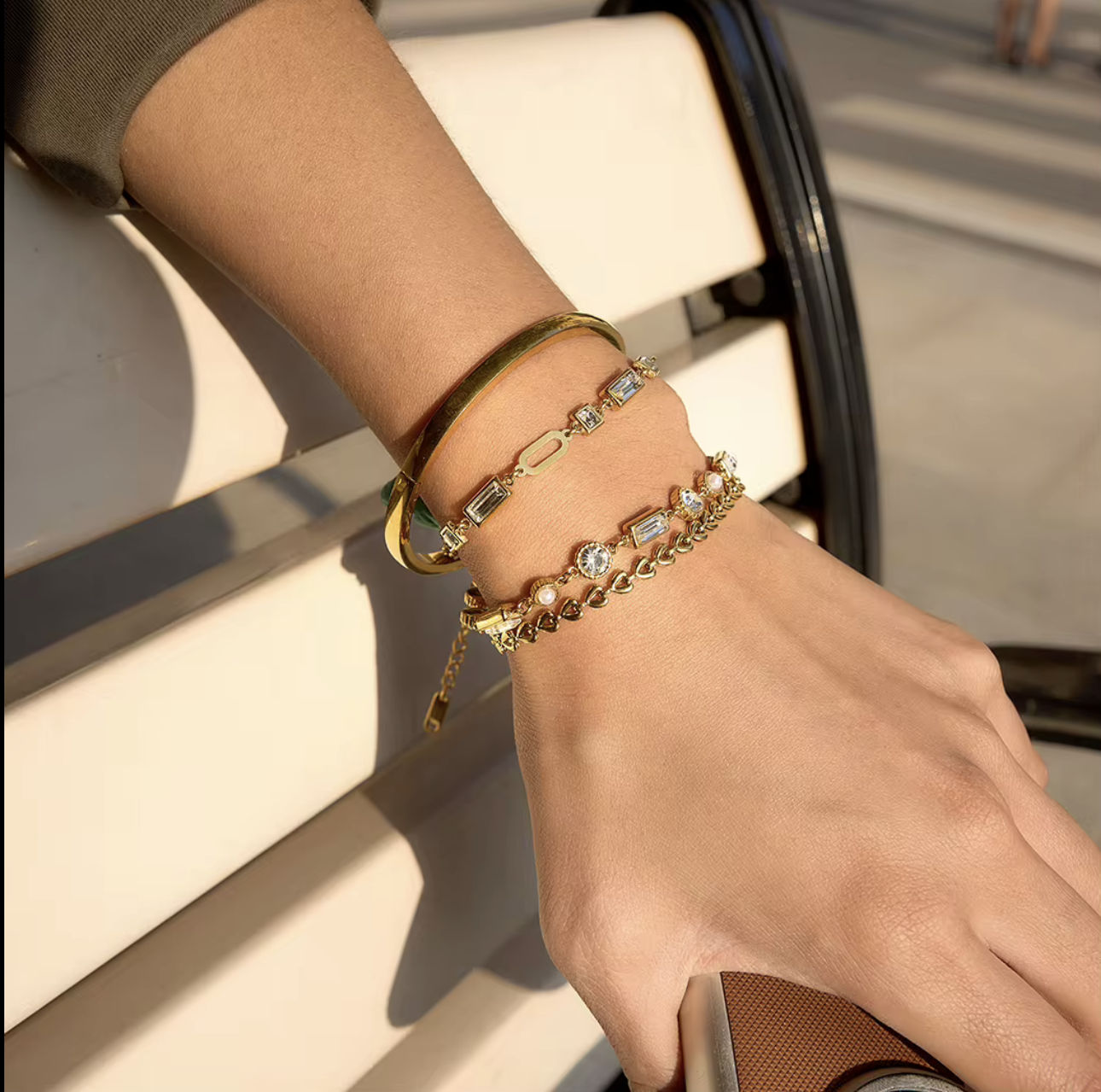 four gold bracelets with gemstones pictured being worn on a wrist