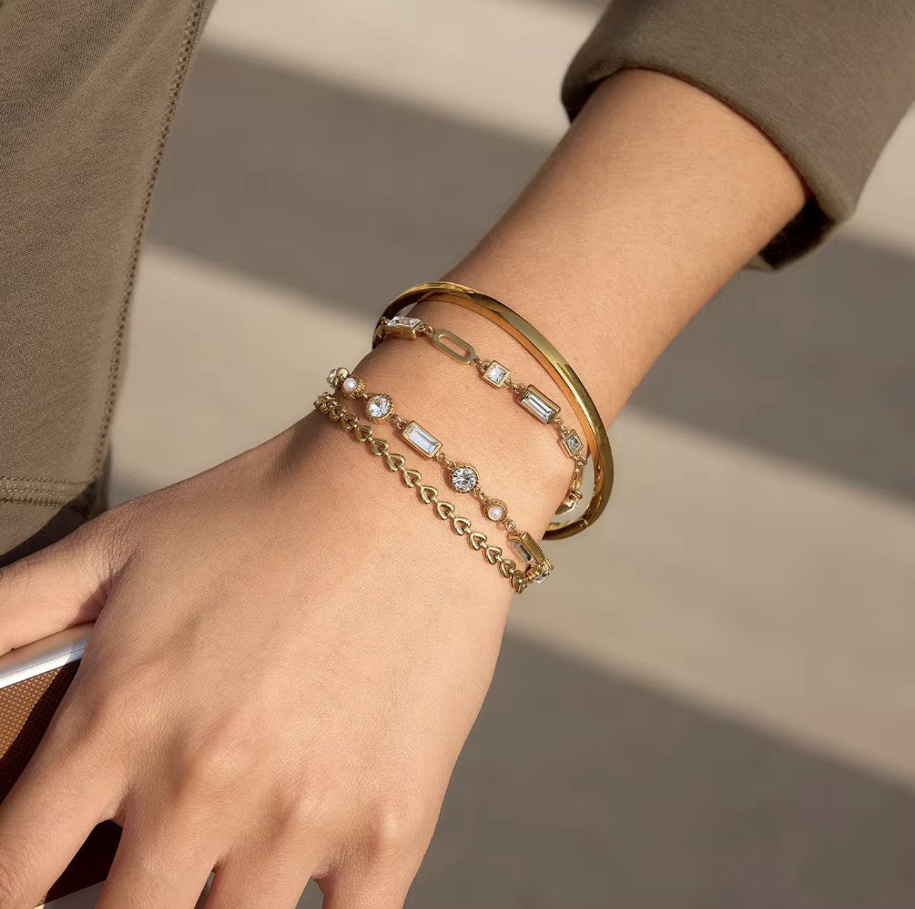 four gold bracelets with gemstones pictured being worn on a wrist