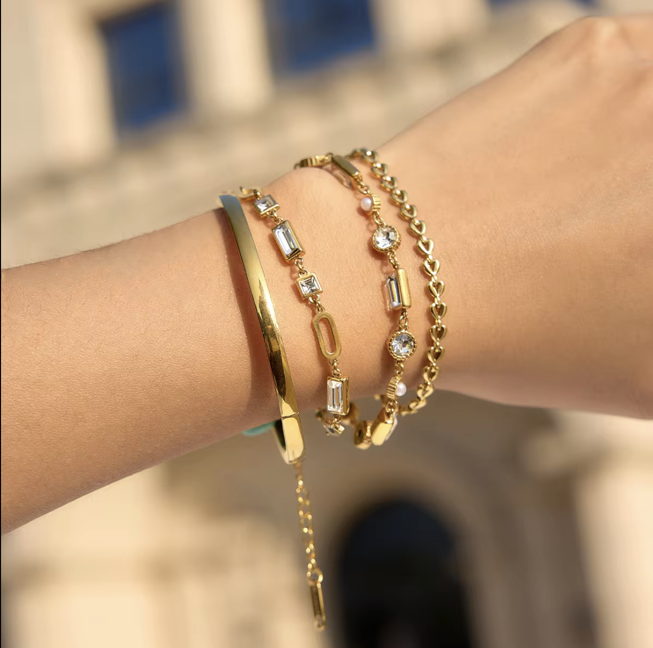four gold bracelets with gemstones pictured being worn on a wrist