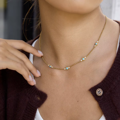 Close-up of a person wearing a gold necklace with small turquoise beads.