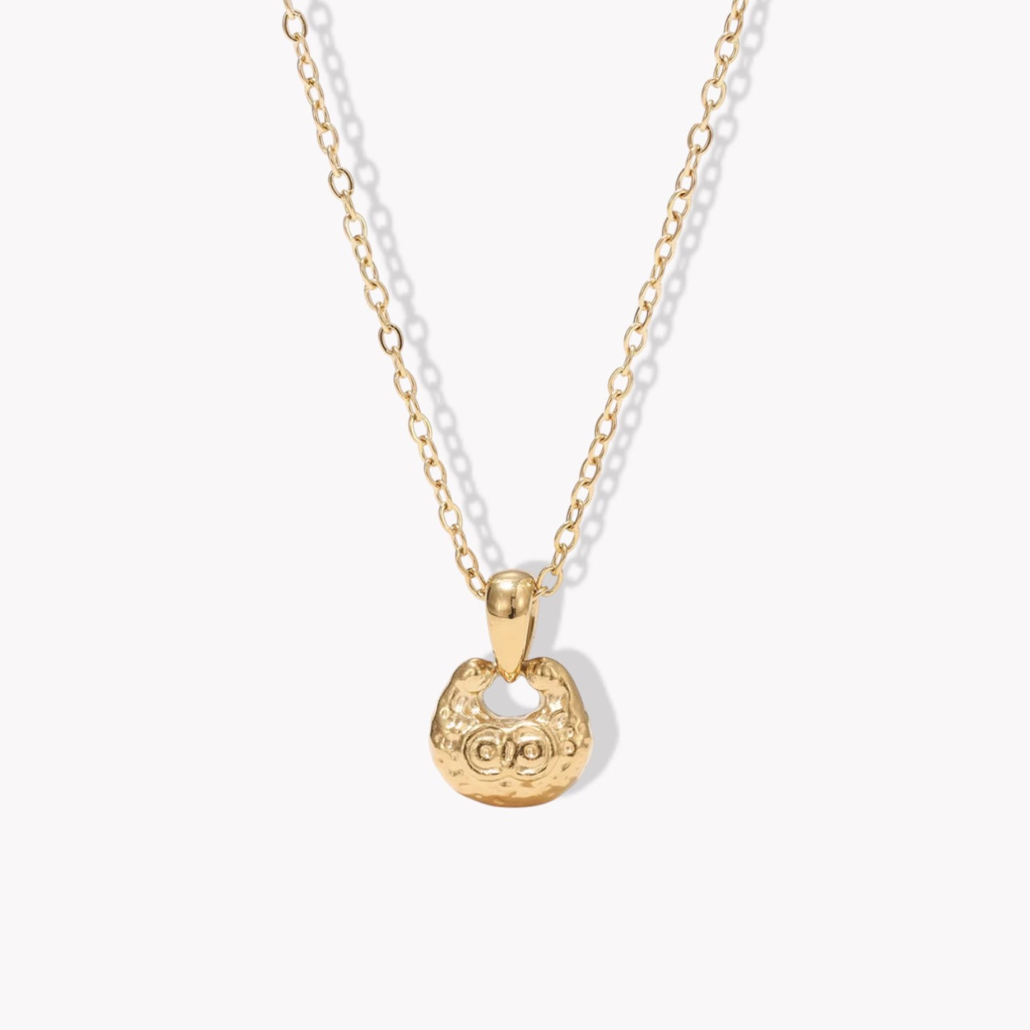 gold necklace featuring small pendant with a textured engave detail pictured on a light background