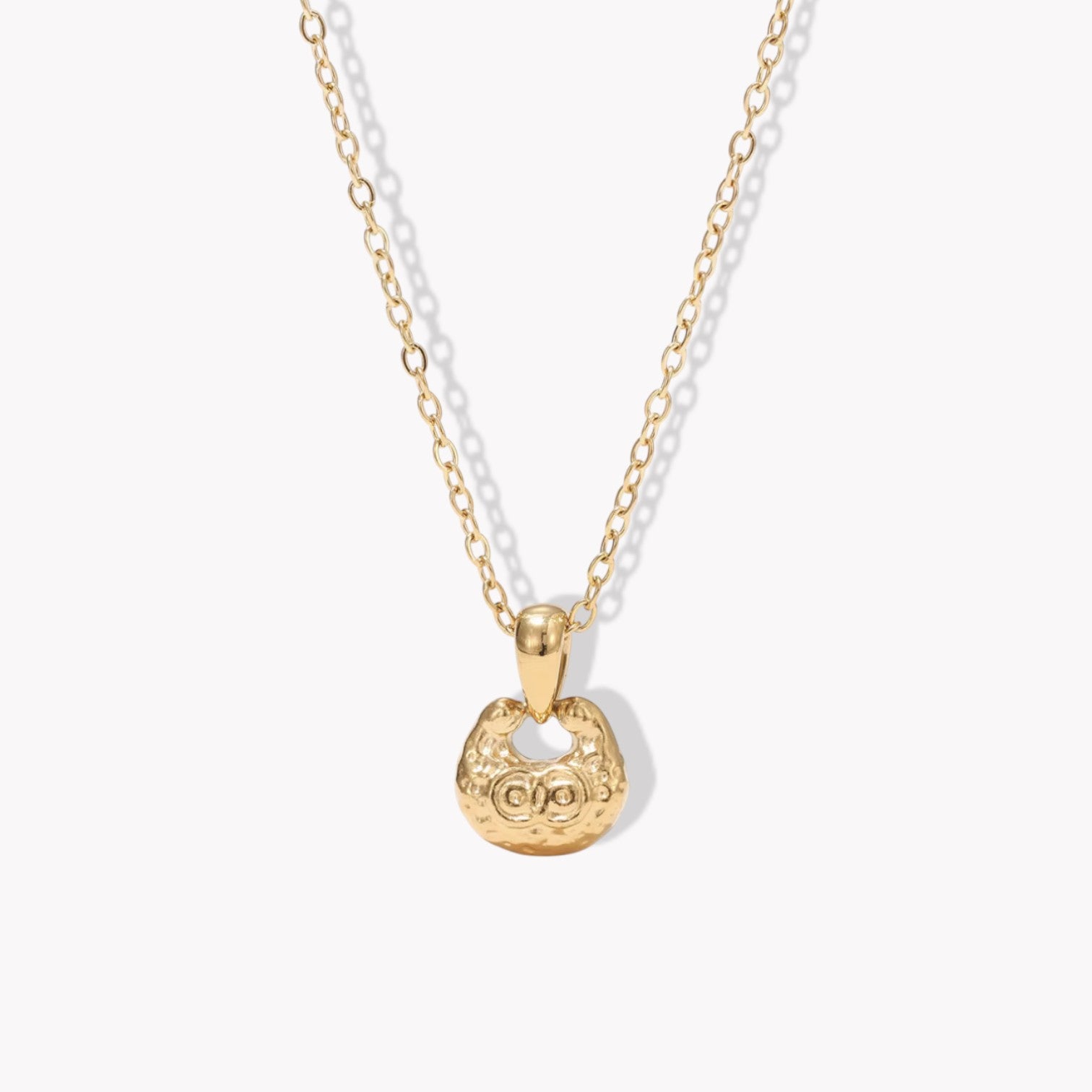 gold necklace featuring small pendant with a textured engave detail pictured on a light background