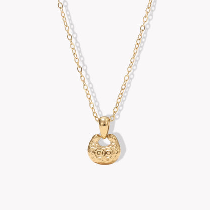 gold necklace featuring small pendant with a textured engave detail pictured on a light background
