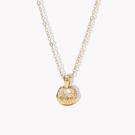 gold necklace featuring small pendant with a textured engave detail pictured on a light background