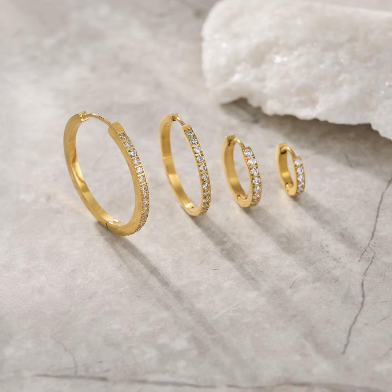 Set of gold hoop earrings with clear stones on a textured surface