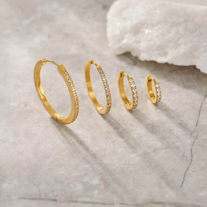 Set of gold hoop earrings with clear stones on a textured surface