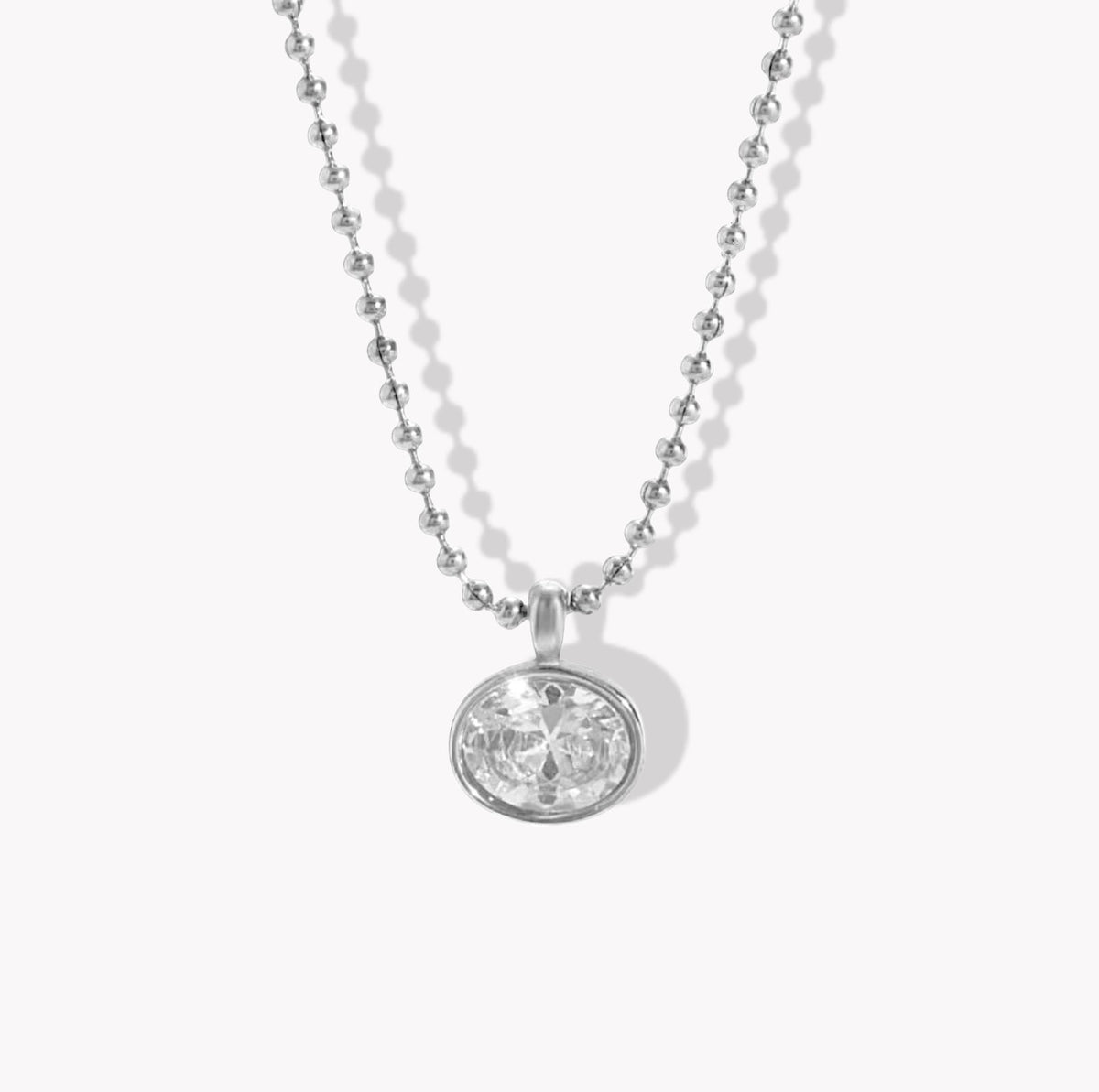A silver ball chain necklace with an oval bezel-set clear gemstone pendant, shown against a light gray background.