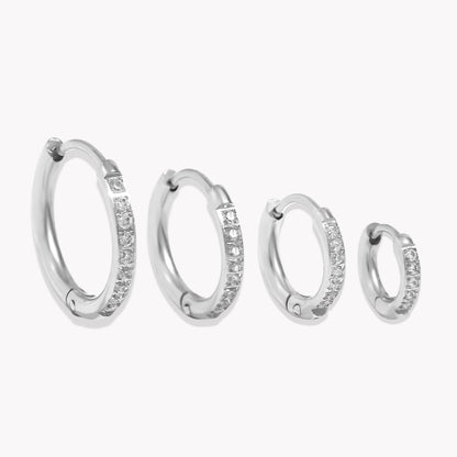 A set of four silver crystal huggie hoop earrings in varying sizes, each with a row of crystals around the hoop.