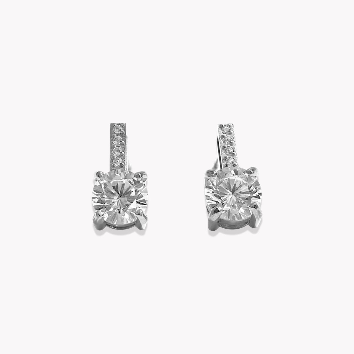 A pair of silver-toned drop earrings with a large round-cut clear center stone and a smaller channel-set row of clear stones above it, shown on a plain light gray background.