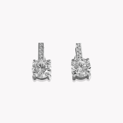 A pair of silver-toned drop earrings with a large round-cut clear center stone and a smaller channel-set row of clear stones above it, shown on a plain light gray background.