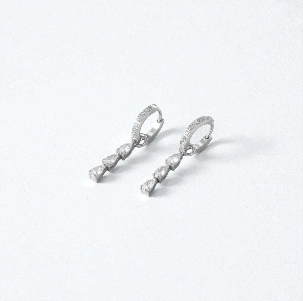 Pair of silver earrings with 3 clear drop pear gemstones on a white background