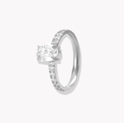 Silver ring with oval gemstone and further gemstones along the band of the ring, pictured on a light grey background