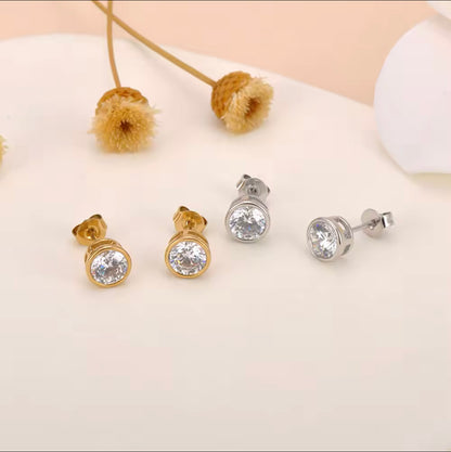 Pair of gold and pair of silver stud earrings both with a rounf gemstone pictured on a neural background with some beige foliage